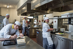 Students preparing food at different stations in training kitchen