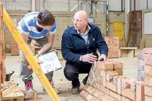 Student and teacher work on decorative brick wall in large workshop