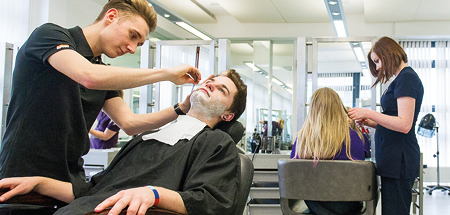 Student uses a straight razor to wet shave a client