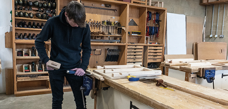 Student working with a mallet and chisel at a work bench to cut a joint in a piece of wood
