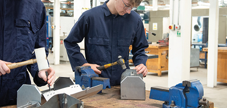Students in a workshop at a work bench, using hand tools to make metal tool boxes