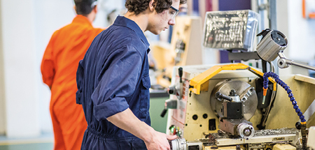 Student in overalls and safety glasses uses a lathe