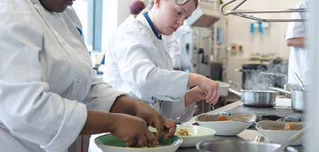 Students in chef’s whites dish up food in a commercial kitchen