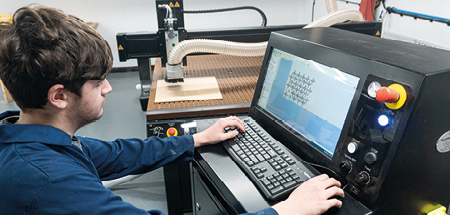 Student programes shapes into a machine’s computer. In the background you can see a router with the cutting arm and extractor over a piece of wood