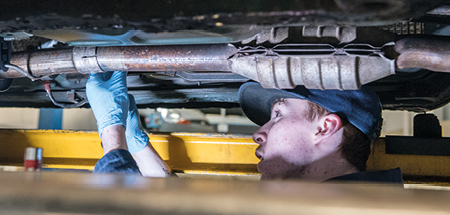 Student under a car, which is up on a lift, working on the exhaust system 