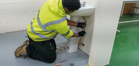 Student in high vis and gloves connects the copper pipes behind a hand basin