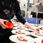 A student places food onto one of a row of beautifully plated pink desserts