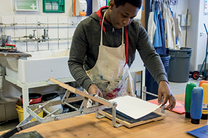 A student at a workbench makes lino prints using a hand press