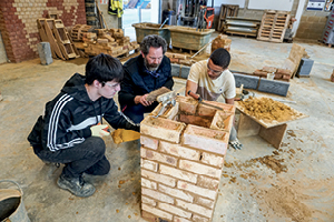 Students and a teacher work on a hollow, square brick pillar
