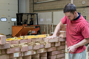 A student places a brick into a decorative pattern that he is creating at the top of a wall