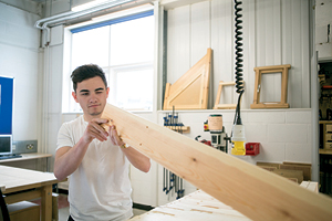 A student works at a work bench examining a long piece of timber