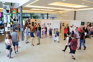 Large exhibition in the Hub with lots of people looking at work displayed on freestanding boards