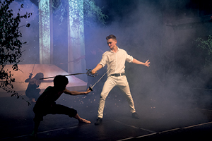 Actors fight on stage with swords, surrounded by smoke