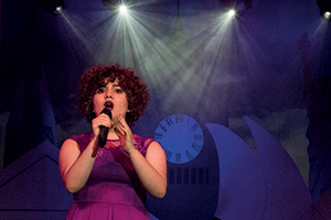 A student sings with hand held microphone under coloured lighting