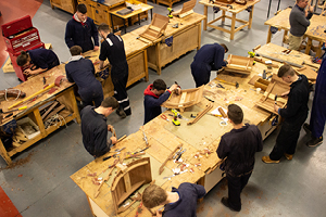 Overhead view of students at workbenches constructing wooden boat sections
