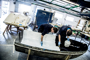 2 students paint the inside of a boat in a large workshop