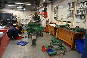 Workshop with various large engines and a group of students stripping down one engine