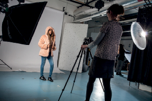 A student photographs a model with studio lighting against a white backdrop