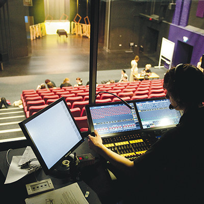 A student works in the sound box at the back of the theatre, the auditorium and stage are in the background